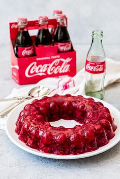 a bundt cake on a plate with coca - cola bottles and spoons next to it