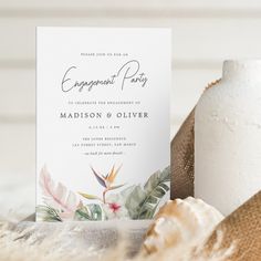 an elegant wedding card with tropical flowers and greenery on it sits next to a vase