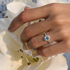 a woman's hand with a ring on it and a flower in the background