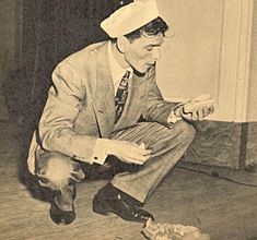 a man in a sailor's hat sitting on the floor looking at his cell phone