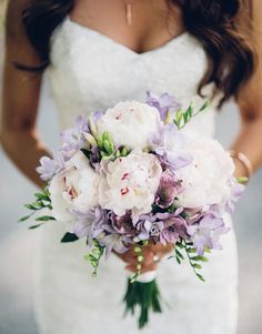 a bride holding a bouquet of white and purple flowers