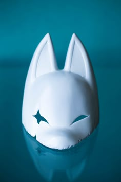 a white cat mask sitting on top of a blue table next to a green wall