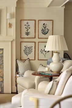 a living room filled with white furniture and pictures on the wall above it's fireplace