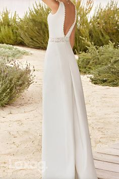 a woman in a long white dress standing on a beach with her back to the camera