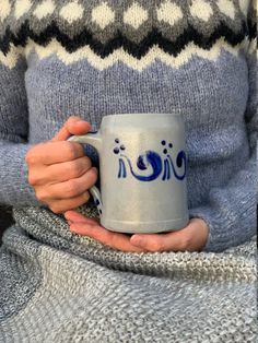 a woman is holding a coffee mug in her hands while wearing a gray and blue sweater