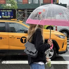 a woman holding an umbrella in the rain on a city street with taxi cabs behind her