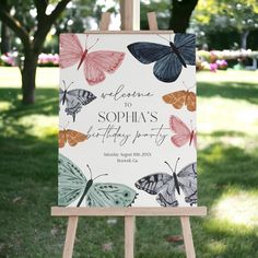 a butterfly themed birthday party sign on an easel in front of some grass and trees