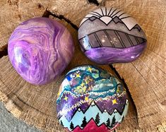 three painted rocks sitting on top of a tree stump