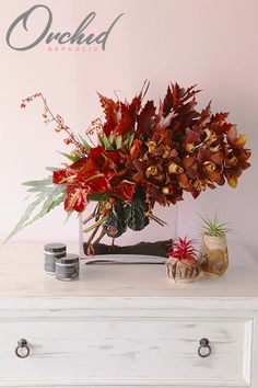 a white dresser topped with a vase filled with lots of red flowers and greenery