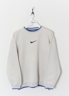 a white sweatshirt with blue trims hangs on a hanger in front of a white wall