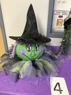 a purple table topped with a green pumpkin wearing a witch hat