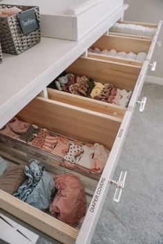 an open drawer with clothes in it on top of a white table and gray carpet