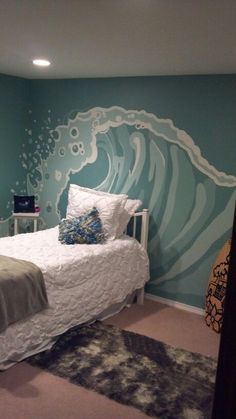 a bedroom decorated in blue and white with an ocean wave painted on the wall behind the bed