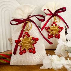 two bags filled with red beads and gold decorations on top of a wooden table next to white flowers