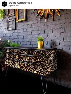 an animal print dresser in front of a brick wall with potted plants on it