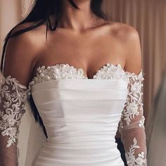 a woman in a white dress with long sleeves and flowers on her arms is posing for the camera