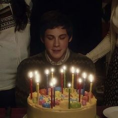 a man sitting in front of a birthday cake with lit candles on top of it