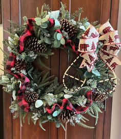 a christmas wreath with pine cones, evergreens and plaid bows hanging on a wooden door