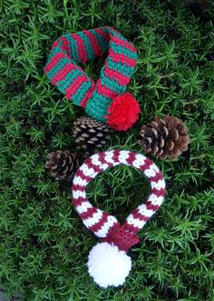 three knitted christmas wreaths and two pine cones on top of some green grass