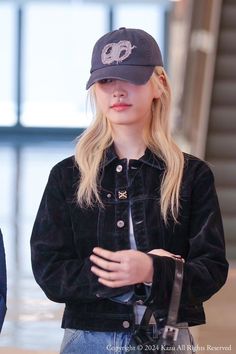 a woman with blonde hair wearing a black jacket and hat standing in front of an airport