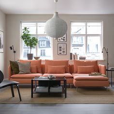 a living room with an orange couch and coffee table in front of two large windows