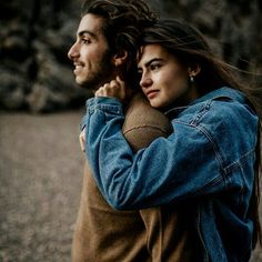 a man and woman embracing each other in front of some rocks with their arms around them