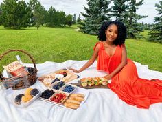 a woman in an orange dress is sitting on a blanket with some food and drinks