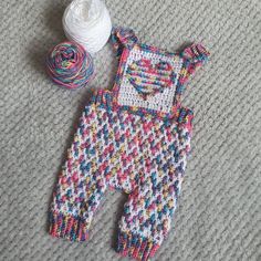 a crocheted baby's outfit next to a ball of yarn on the floor