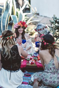 four women sitting around a table with drinks and flowers in their hair, all wearing flower crowns