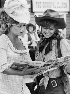 two women in hats are looking at a newspaper