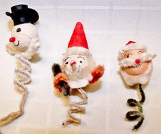 three small christmas ornaments are sitting on a white tablecloth, one is wearing a santa hat and the other has two mice