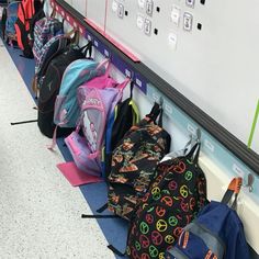 several backpacks lined up against the wall in a school hallway, all with peace signs on them