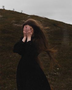 a woman covers her face with her hands as she stands on the side of a hill