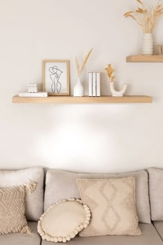 a couch with some pillows on top of it next to two bookshelves and vases