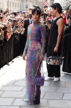 a woman in a colorful dress is walking down the street while people are taking pictures