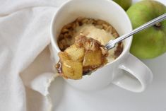 a spoon with some food in it on a white plate next to two green apples