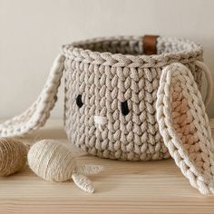 a crocheted basket sitting on top of a wooden table next to two balls of yarn