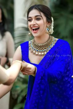 a woman in a blue sari smiles as she holds her hand out to another woman