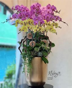 purple and yellow orchids in a gold vase on a black table with greenery