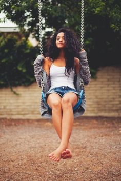 a woman sitting on a swing in the middle of a park with her feet up