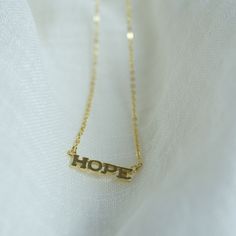 This elegant "hope" necklace is a symbol of positivity and strength. Crafted from high-quality 14k gold plated silver, it features a unique design with a center piece and two loops on either side. The necklace is 16 inches in length with a 1-inch extension, allowing for adjustable wear. Finished with a lobster clasp, this necklace is both stylish and versatile, making it a perfect addition to any outfit. Details: Material: 14k gold plated silver  Necklace length: 16 inches with 1-inch extension Design: "HOPE' is 20mm long 5mm wide and 1mm thick  Closure: Lobster clasp Hypoallergenic: Yes Nickel-free: Yes Handcrafted: Yes Hope Necklace, Extension Designs, Necklace Layering, Gold Necklace Layered, Layering Necklace, Gold Plated Silver, 14kt Gold, Necklace Length, Name Necklace