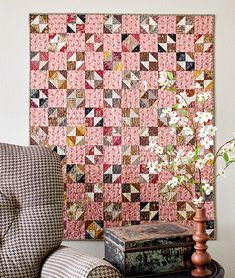 a living room with a chair and a quilt on the wall behind it, next to a vase with flowers