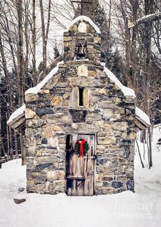 an old stone building with a wreath on the door and snow covered ground around it