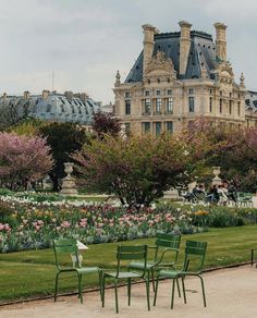 three green chairs sitting in the middle of a flower garden with a large building in the background