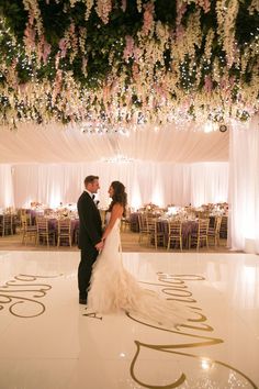 a bride and groom standing on the dance floor in front of an elaborately decorated ceiling