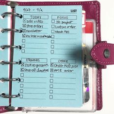 a pink and blue planner is open on a white surface with a red clipboard attached to it