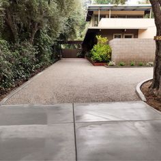 a driveway with gravel and trees in front of a house that has a large tree on the side