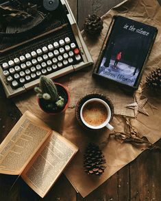 an old typewriter, cup of coffee and book on a table with pine cones