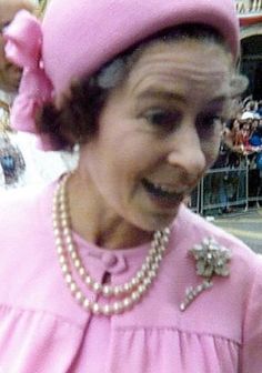 an older woman in a pink dress and hat with pearls on her head is smiling for the camera