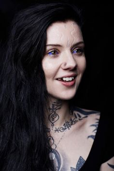 a woman with tattoos on her chest posing for a photo in front of a black background